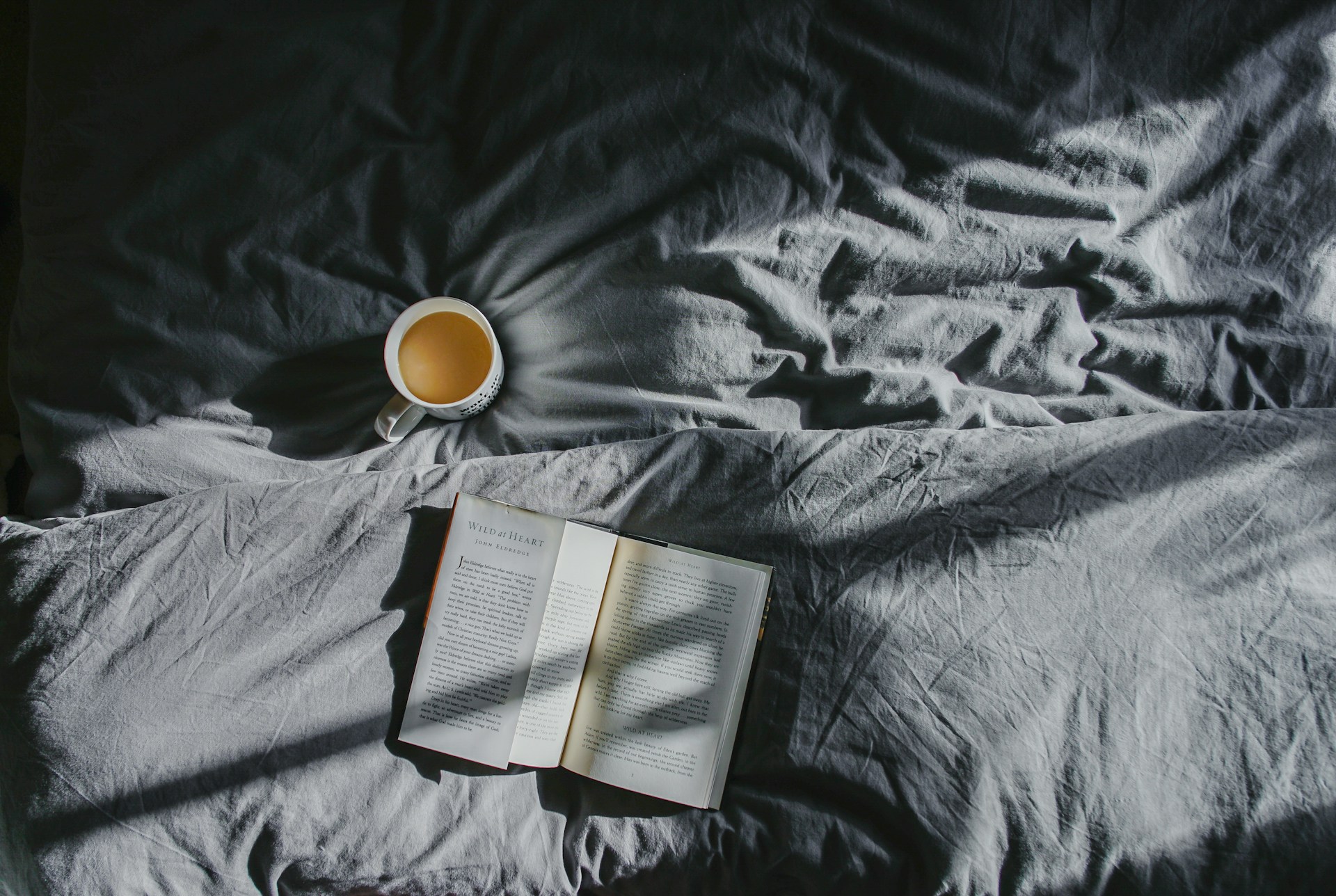 A cup of coffee and a book on a bed